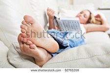 stock-photo-barefoot-young-woman-lying-on-sofa-and-reading-book-shallow-depth-of-field-focus-on-.jpg